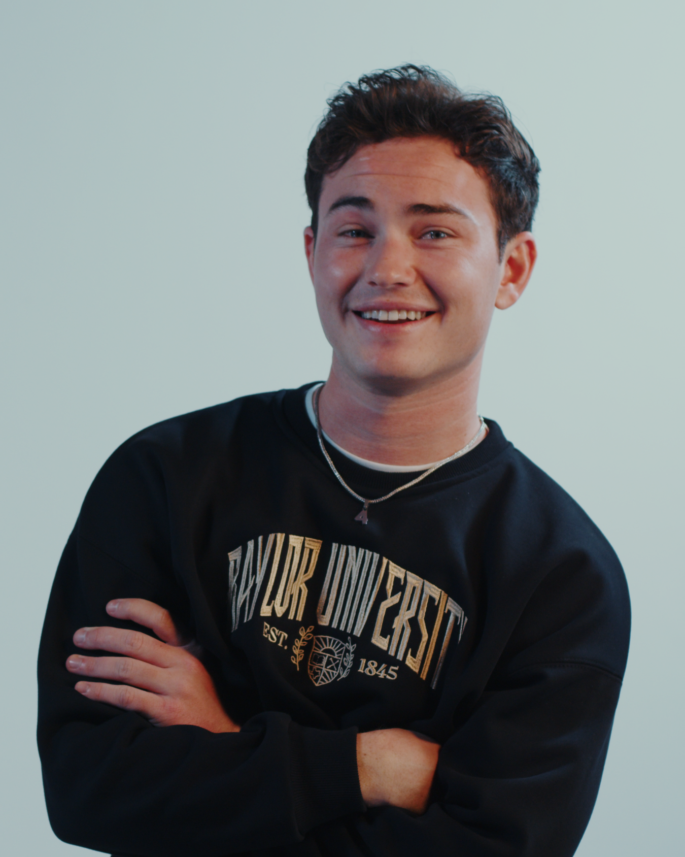 Man smiling wearing a black embroidered Baylor University sweatshirt on a white background