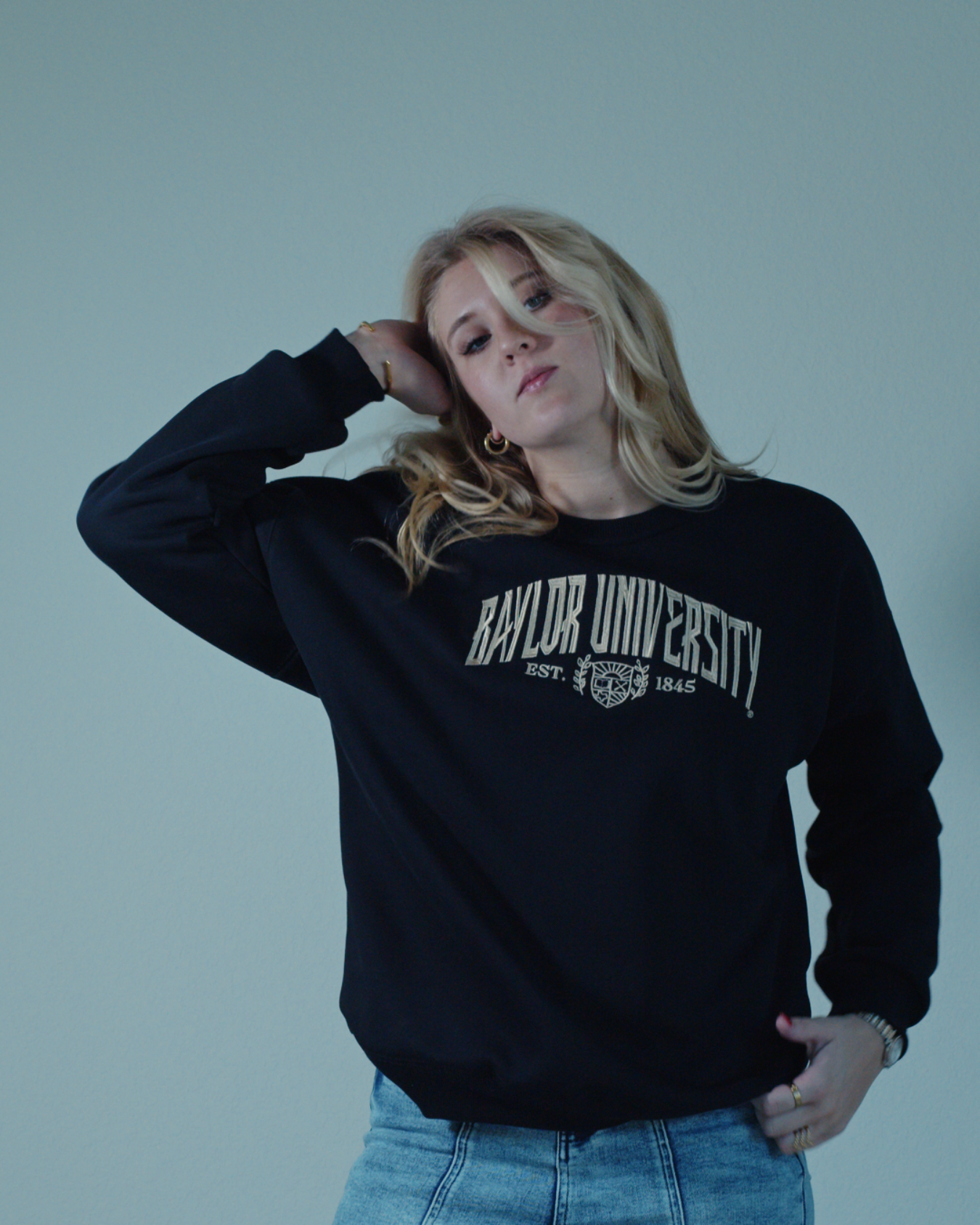 Blonde girl wearing a black embroidered Baylor University crewneck sweatshirt on a white background