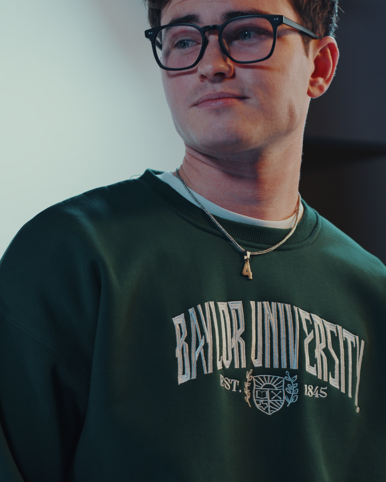 Hot male model guy with glasses wearing a forrest green Baylor University embroidered sweatshirt crewneck in a studio with a white background