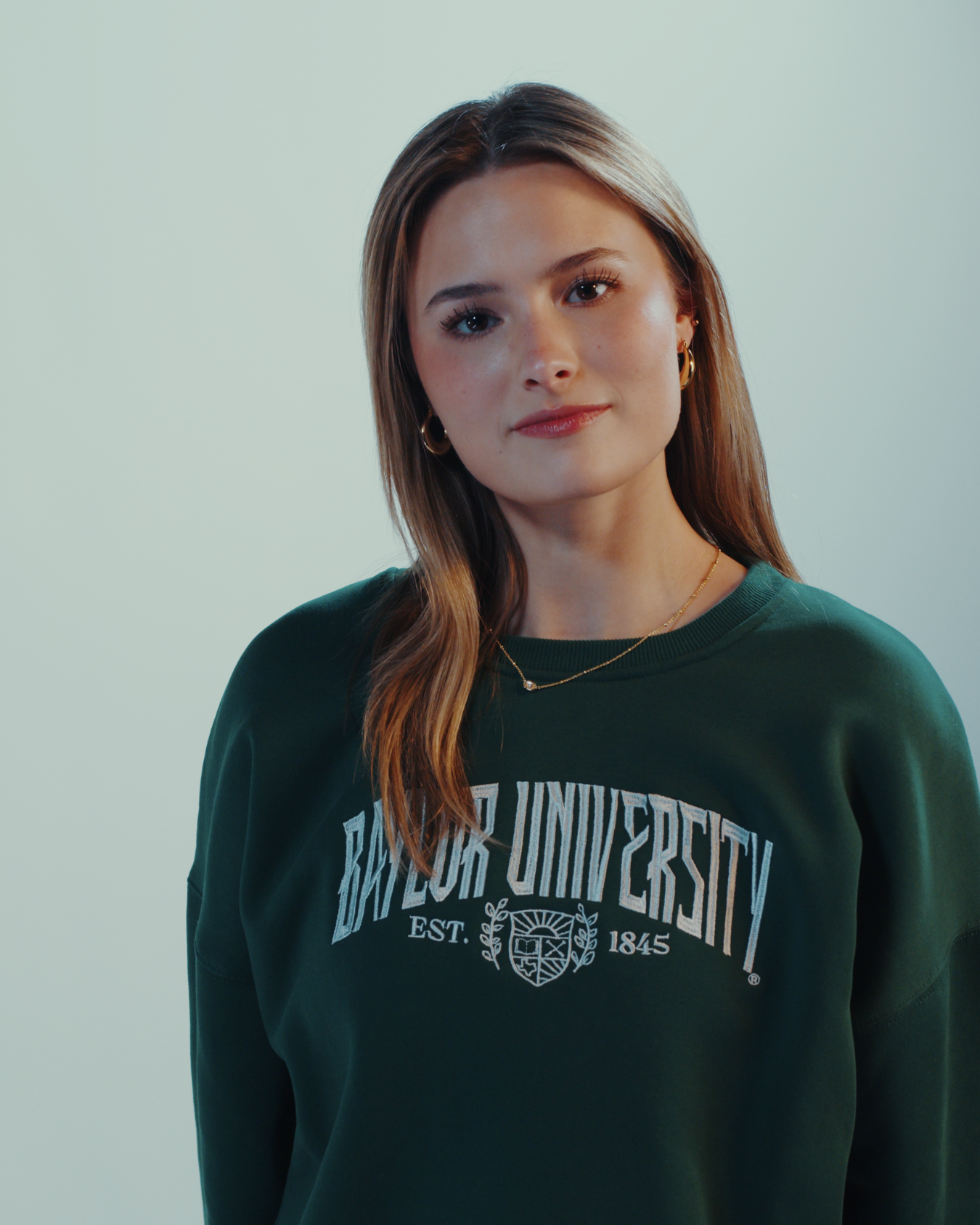 Beautiful girl wearing a green embroidered Baylor University sweatshirt crewneck on a white background