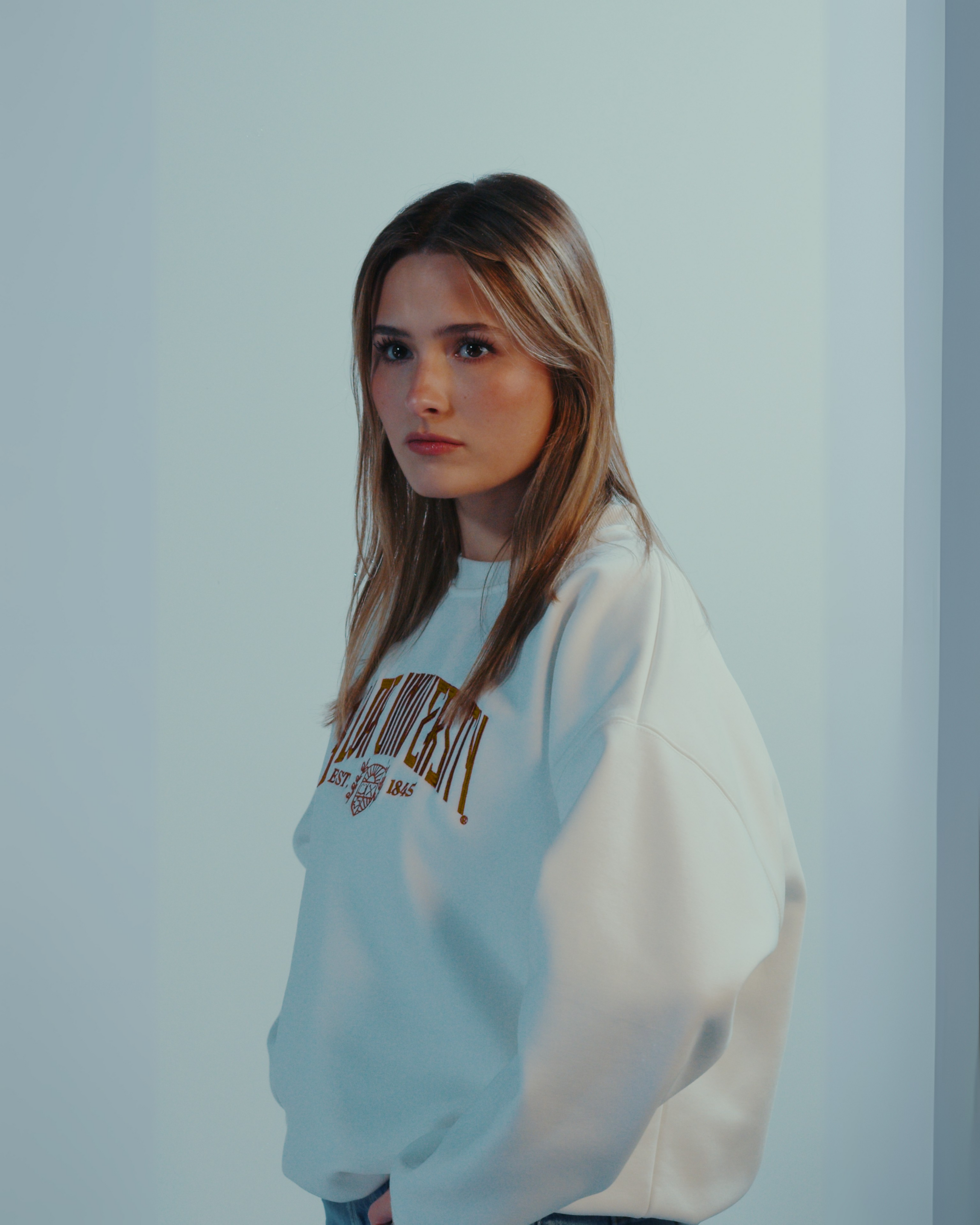 Woman wearing a white sweatshirt with the text Baylor University against a plain background