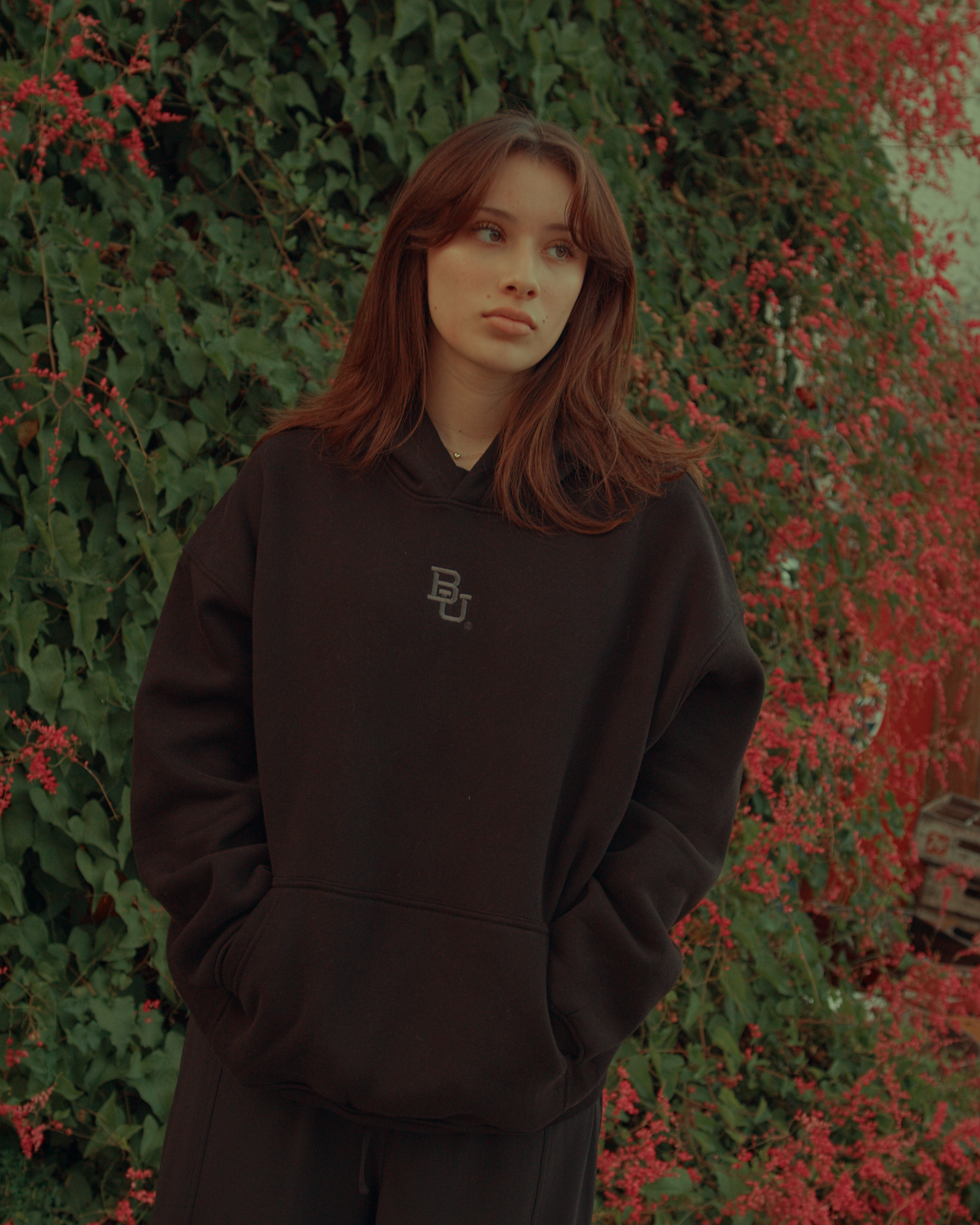 Girlwearing a black Baylor University hoodie with a logo in front of a green and red leafy background