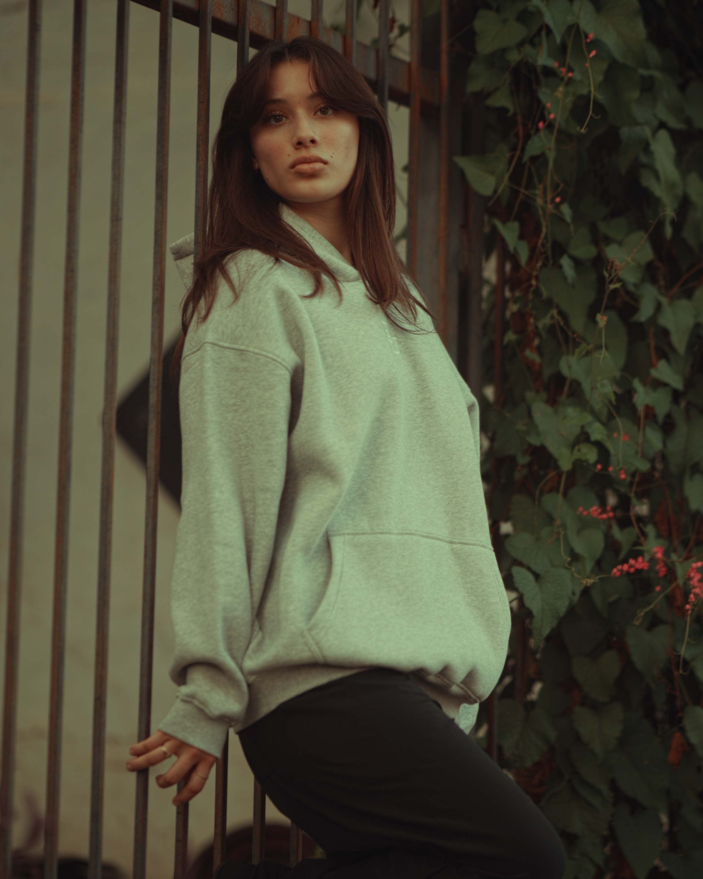 Girl wearing a light gray Baylor hoodie standing outdoors with greenery in the background