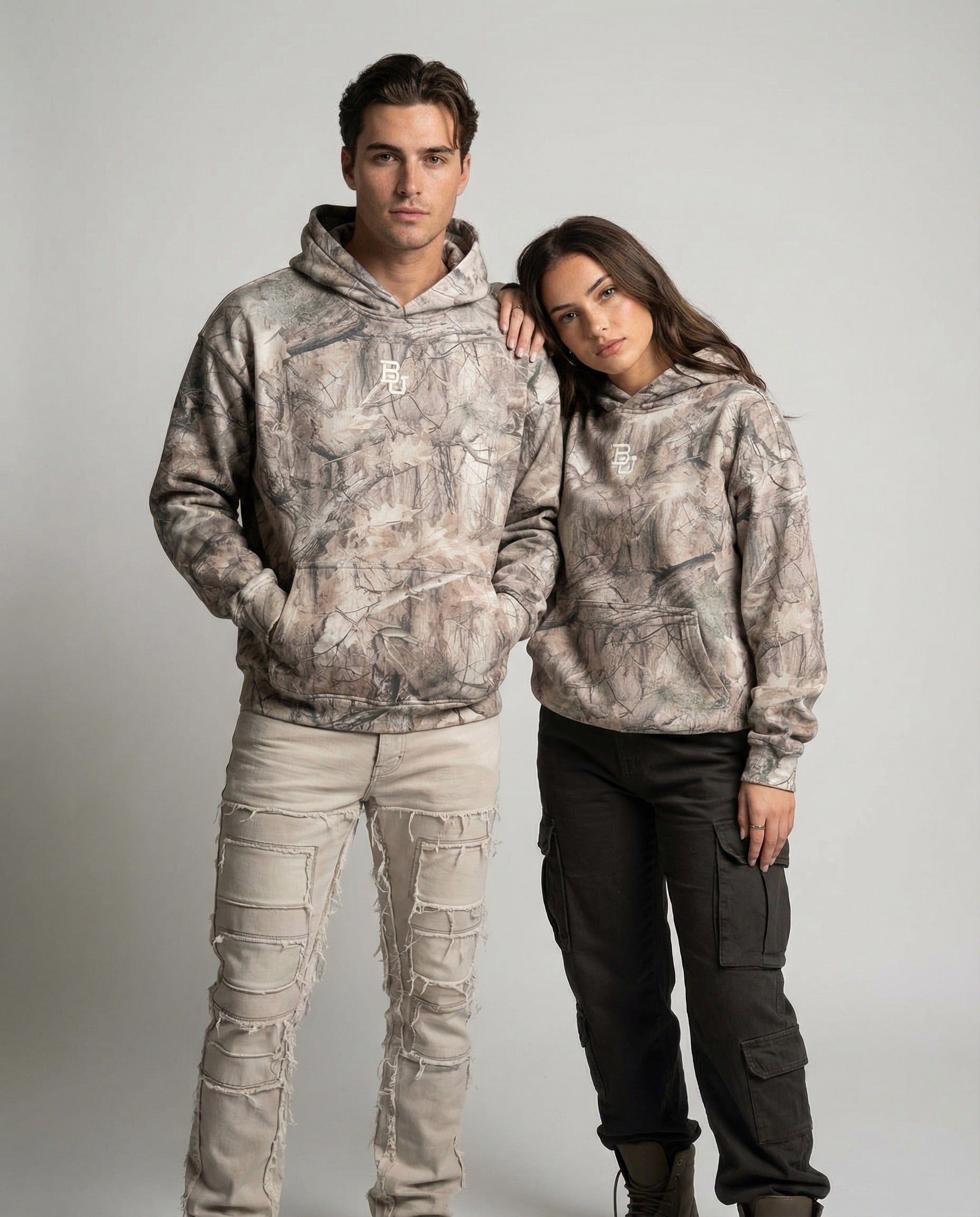 Two people wearing Baylor camouflage hoodies and pants on a plain background
