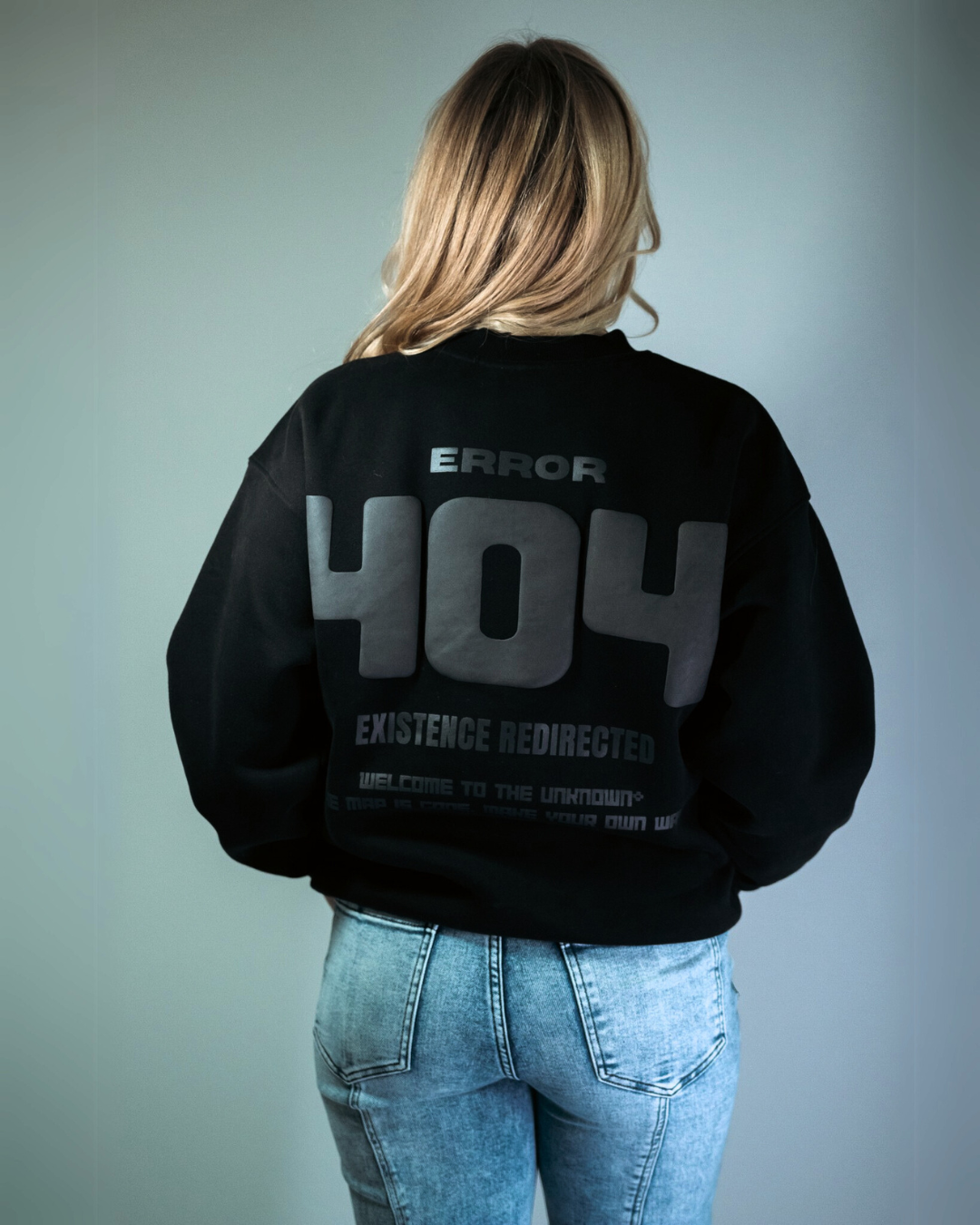 blonde model wearing a black sweatshirt that says 'Error 404, existence redirected' on a studio white background