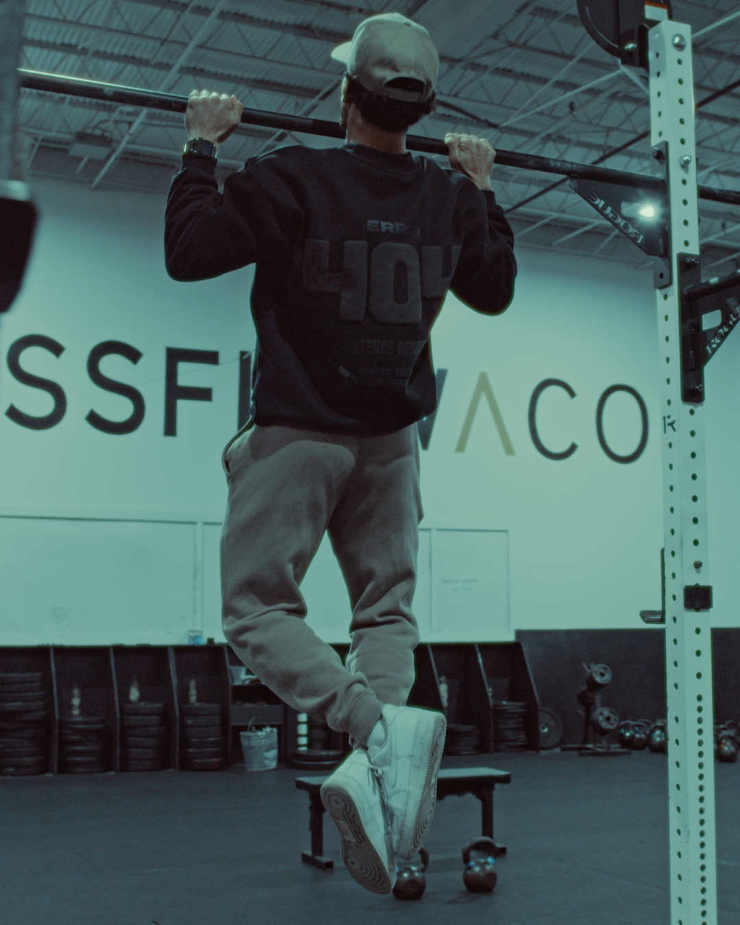 man doing pullups in a gym wearing a zoleado black crewneck it reads 'error 404'