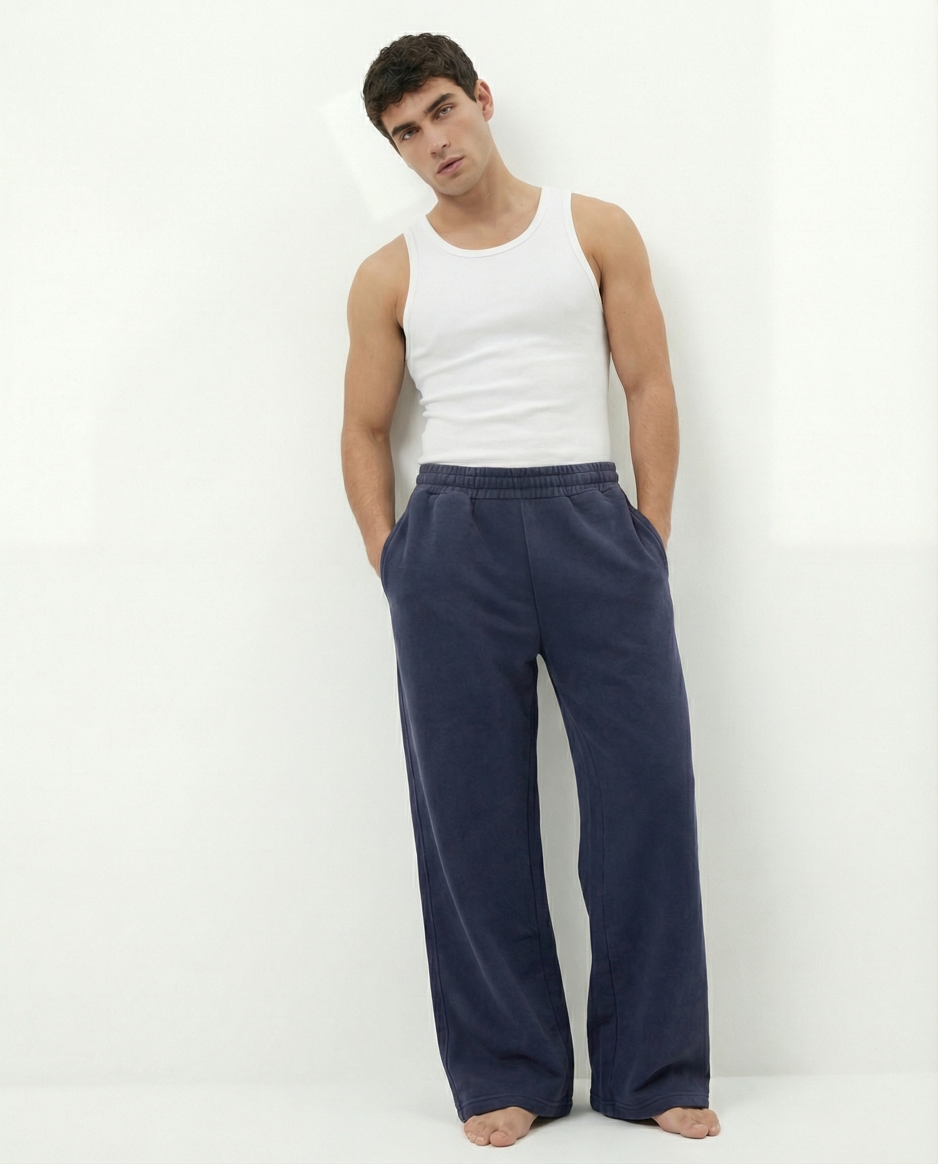 Man wearing a white tank top and blue acid wash pants on a white background