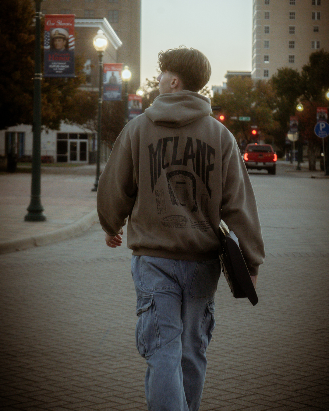 Tall male model holding a keyboard wearing the olive green Baylor University mclane stadium heavyweight cotton hoodie walking down the street with a keyboard piano