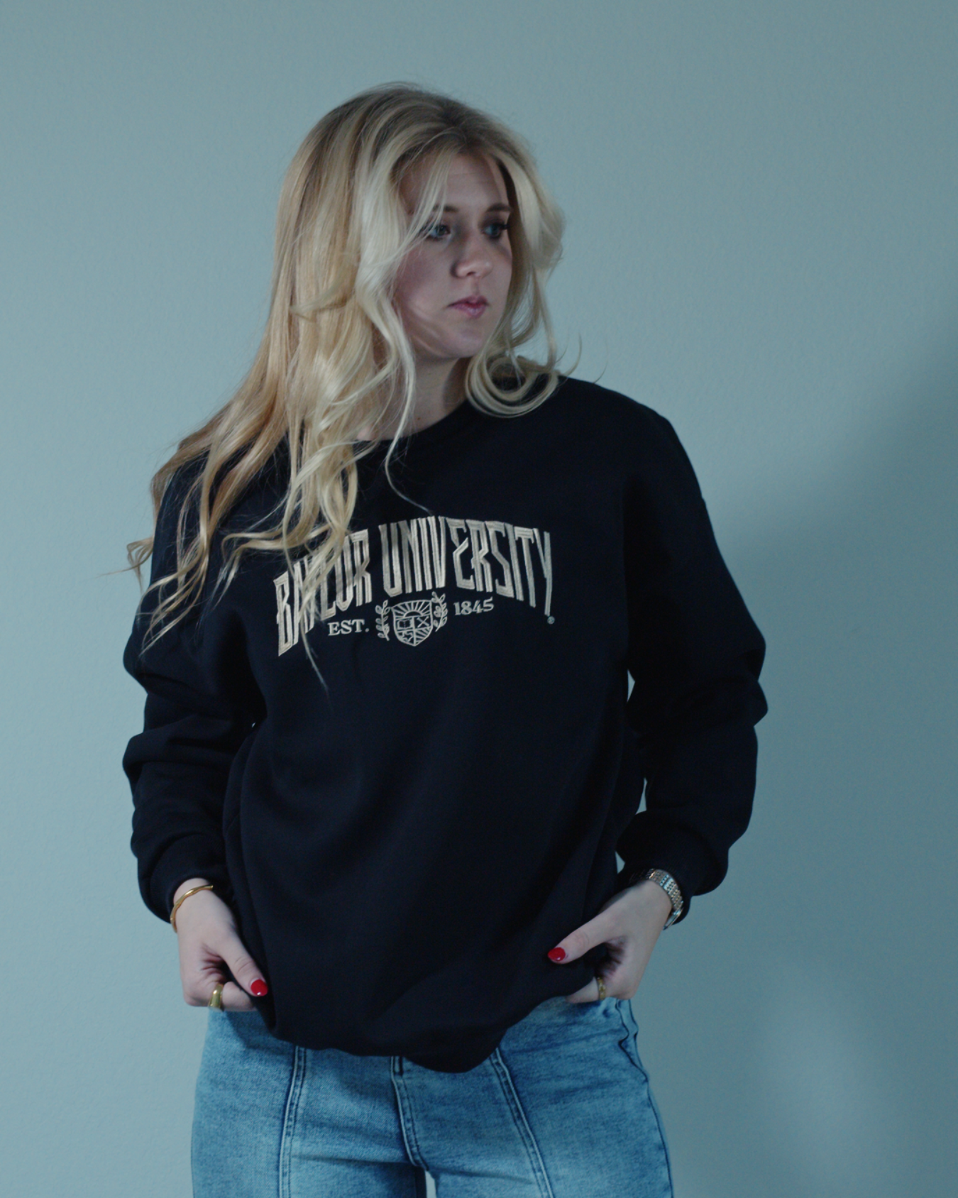 Blonde girl on a white background wearing a black embroidered Baylor University sweatshirt crewneck