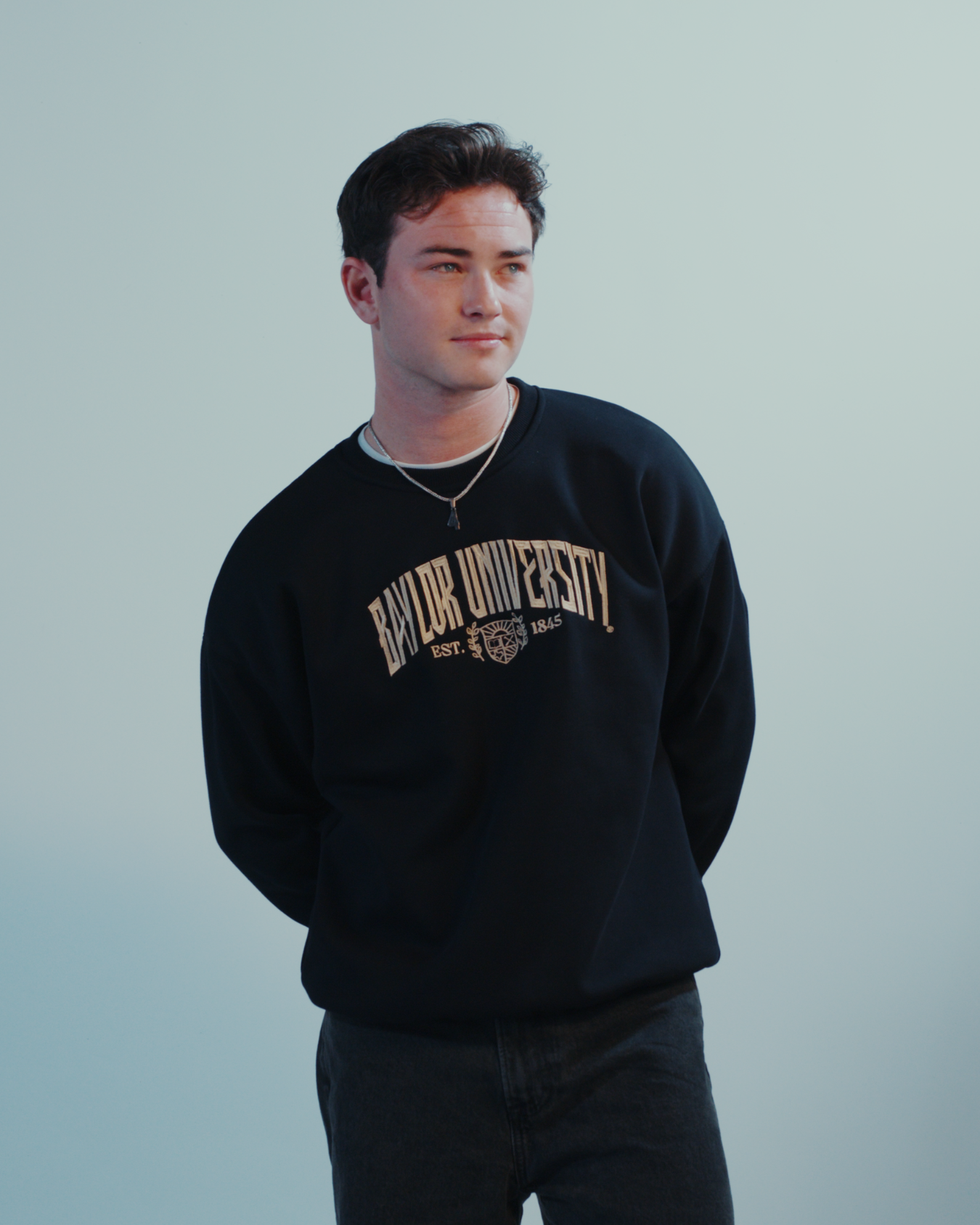 Man wearing a black embroidered Baylor University crewneck sweatshirt on a white background
