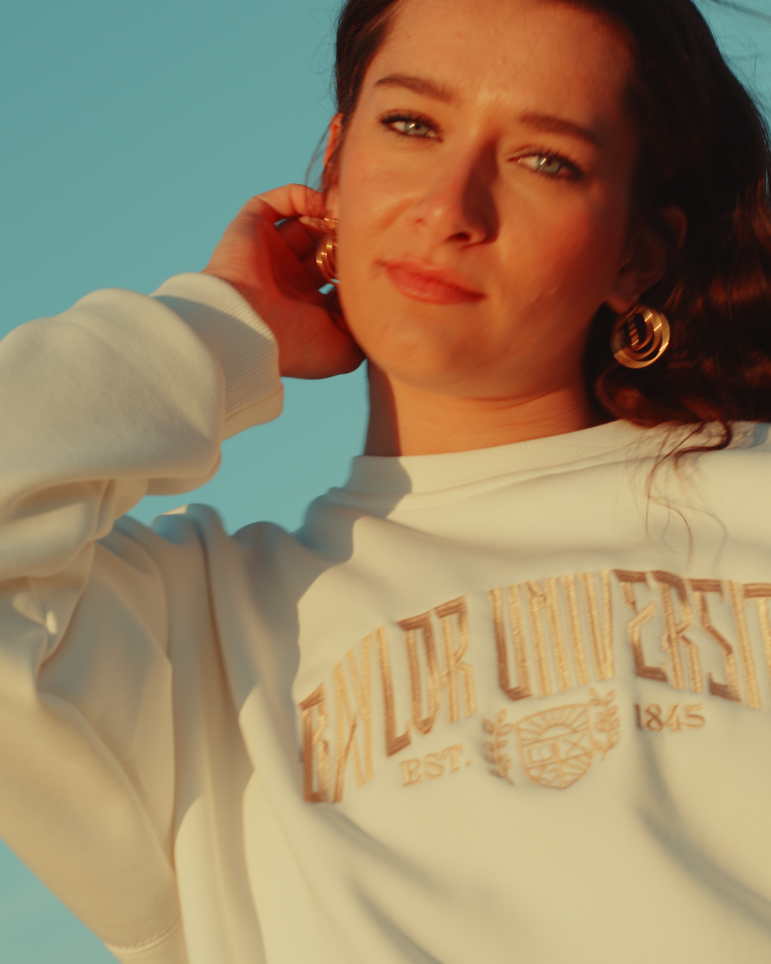 woman wearing a Baylor University crewneck sweatshirt outside with a blue sky background