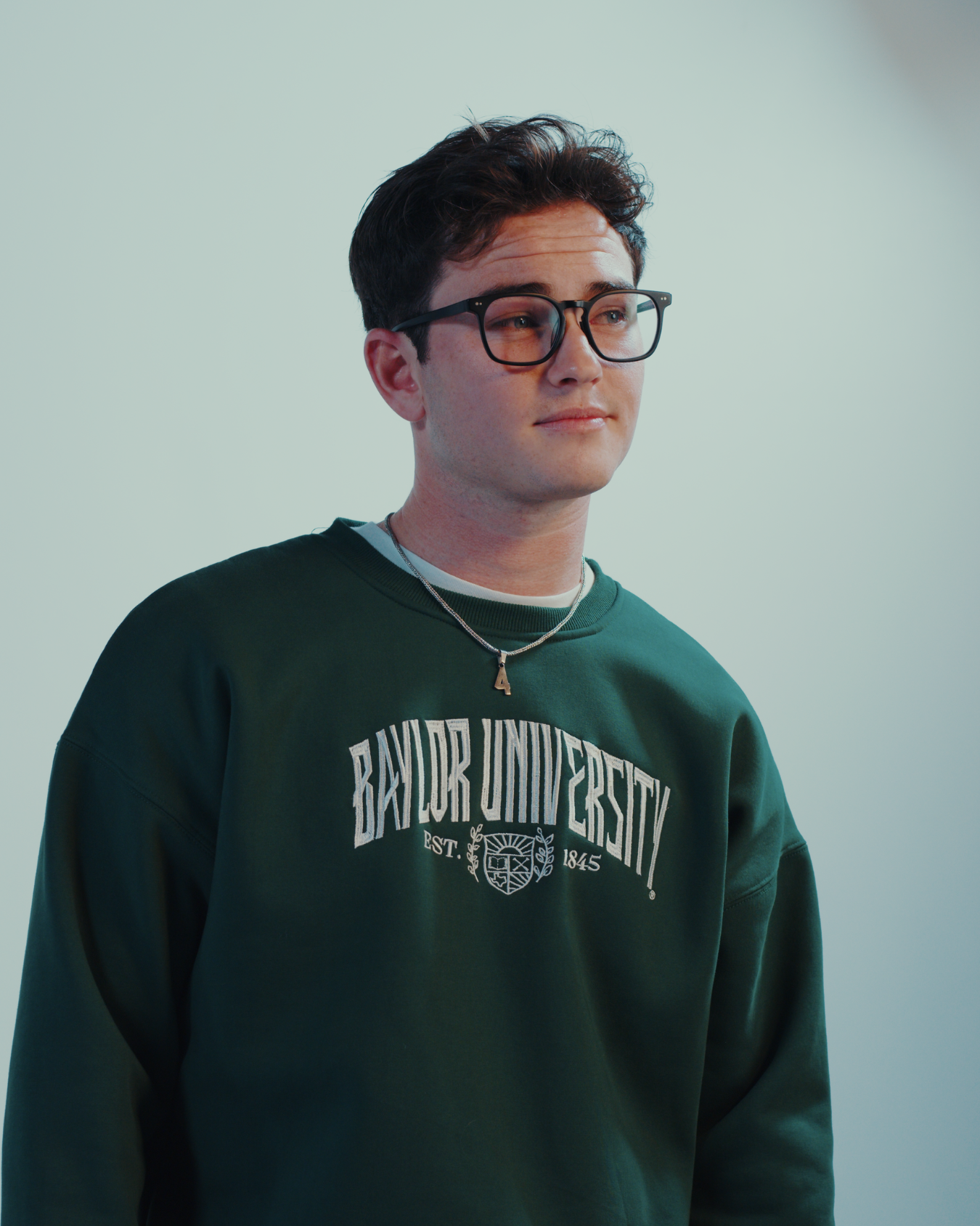 Hot male model with glasses wearing a green embroidered Baylor University sweatshirt crewneck
