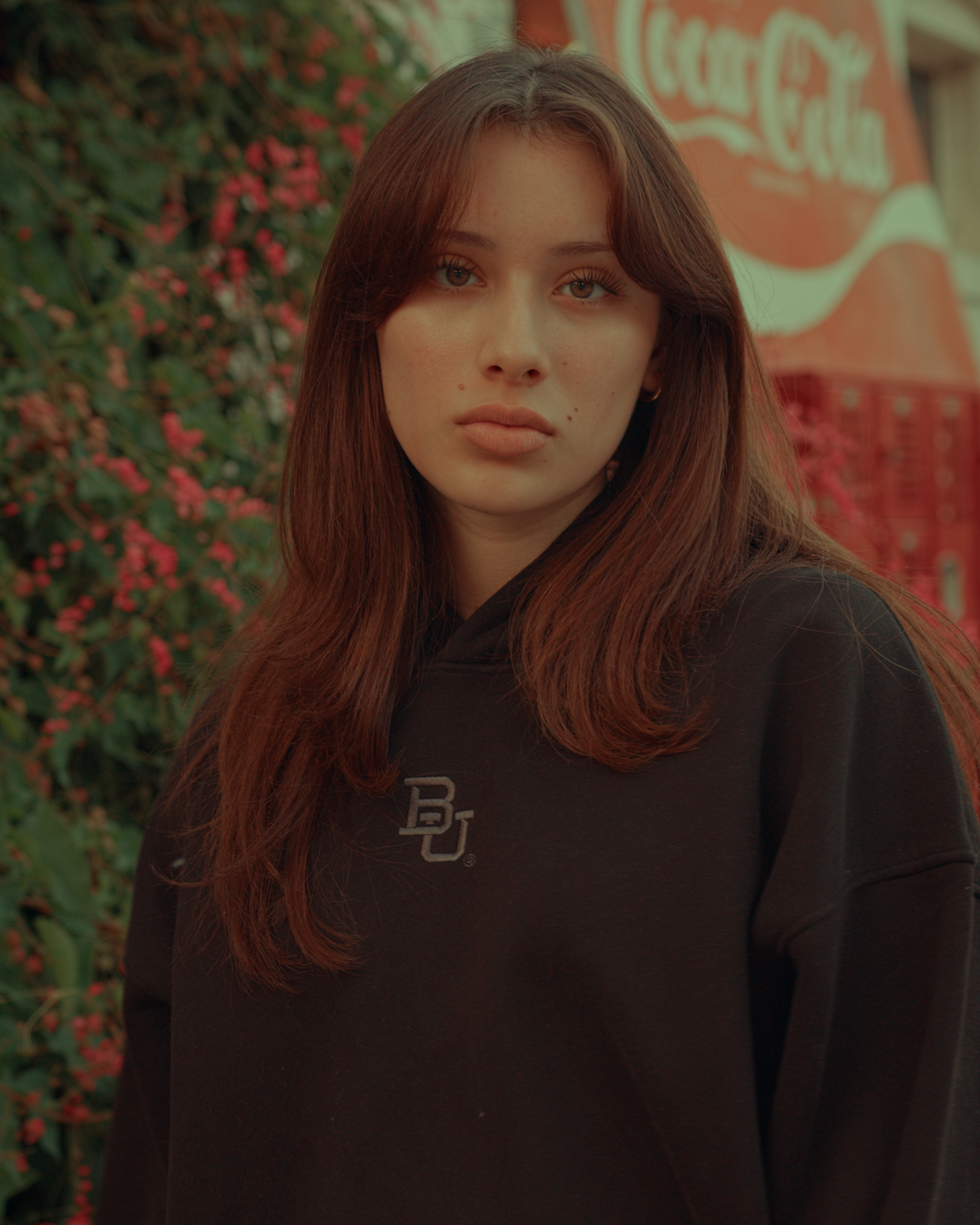 girl wearing a black Baylor University hoodie with a logo in front of a Coca-Cola sign