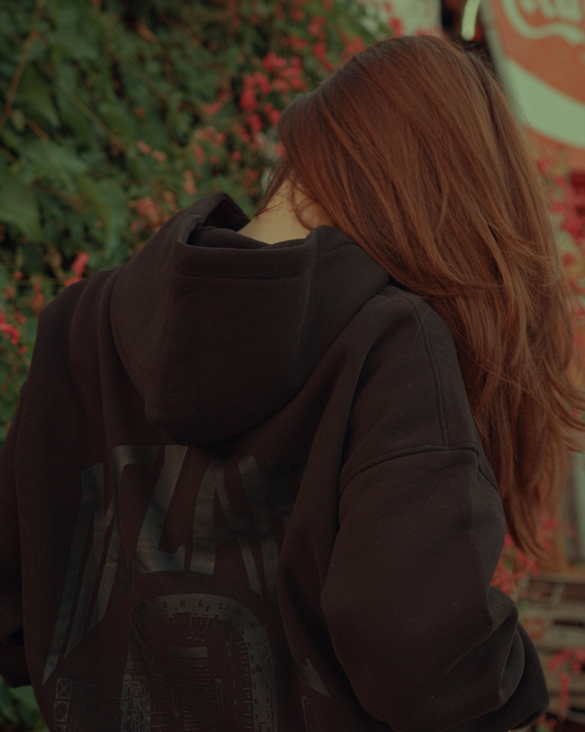 Woman wearing a dark hoodie with a backpack, standing in front of green foliage. Baylor University hoodie