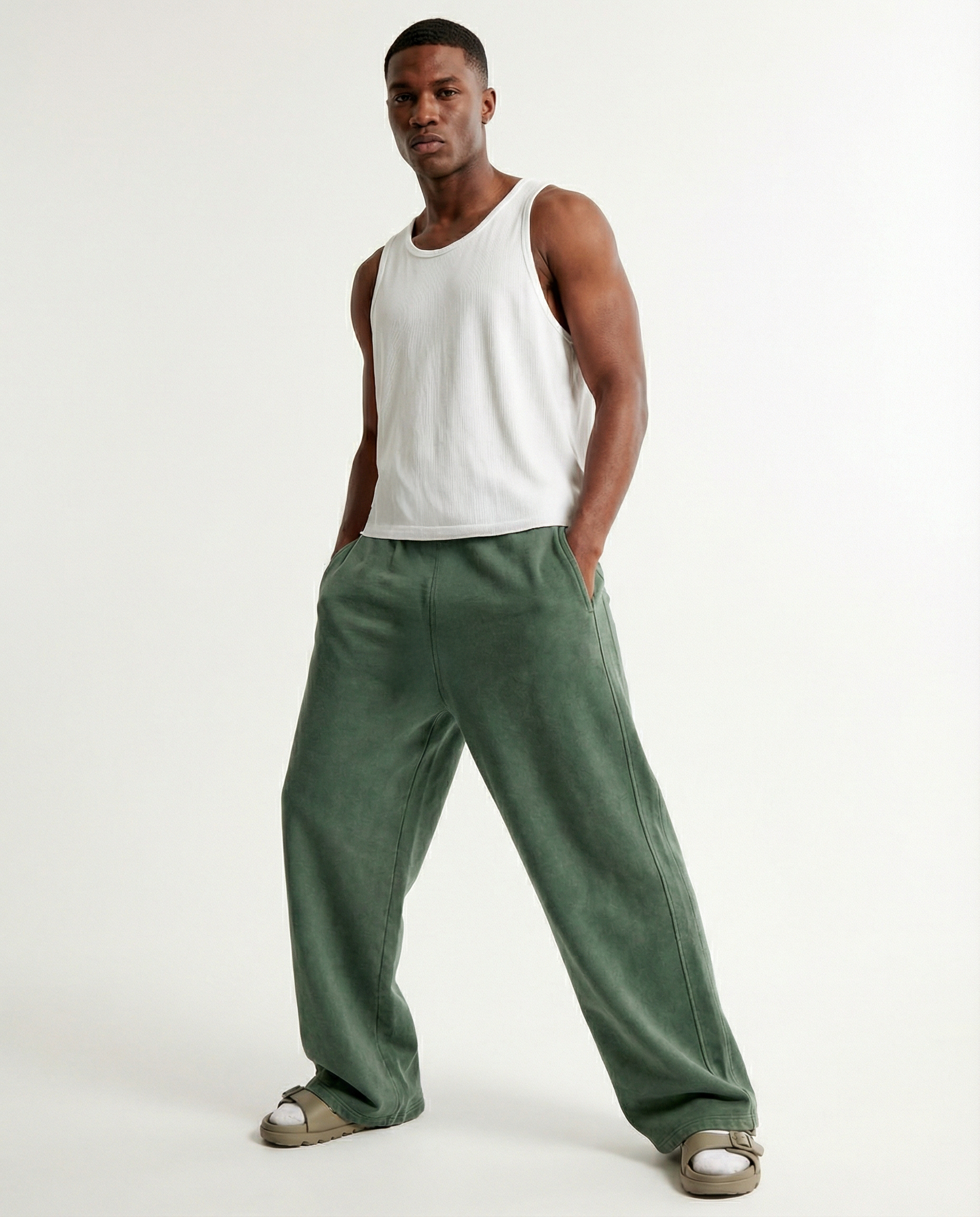 Black man wearing a white tank top and green acid wash pants on a white background