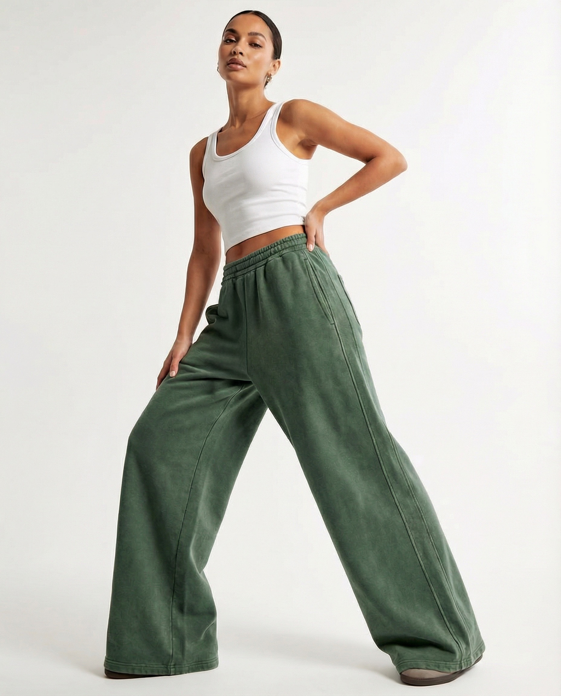 Woman wearing green wide-leg pants and a white tank top on a white background