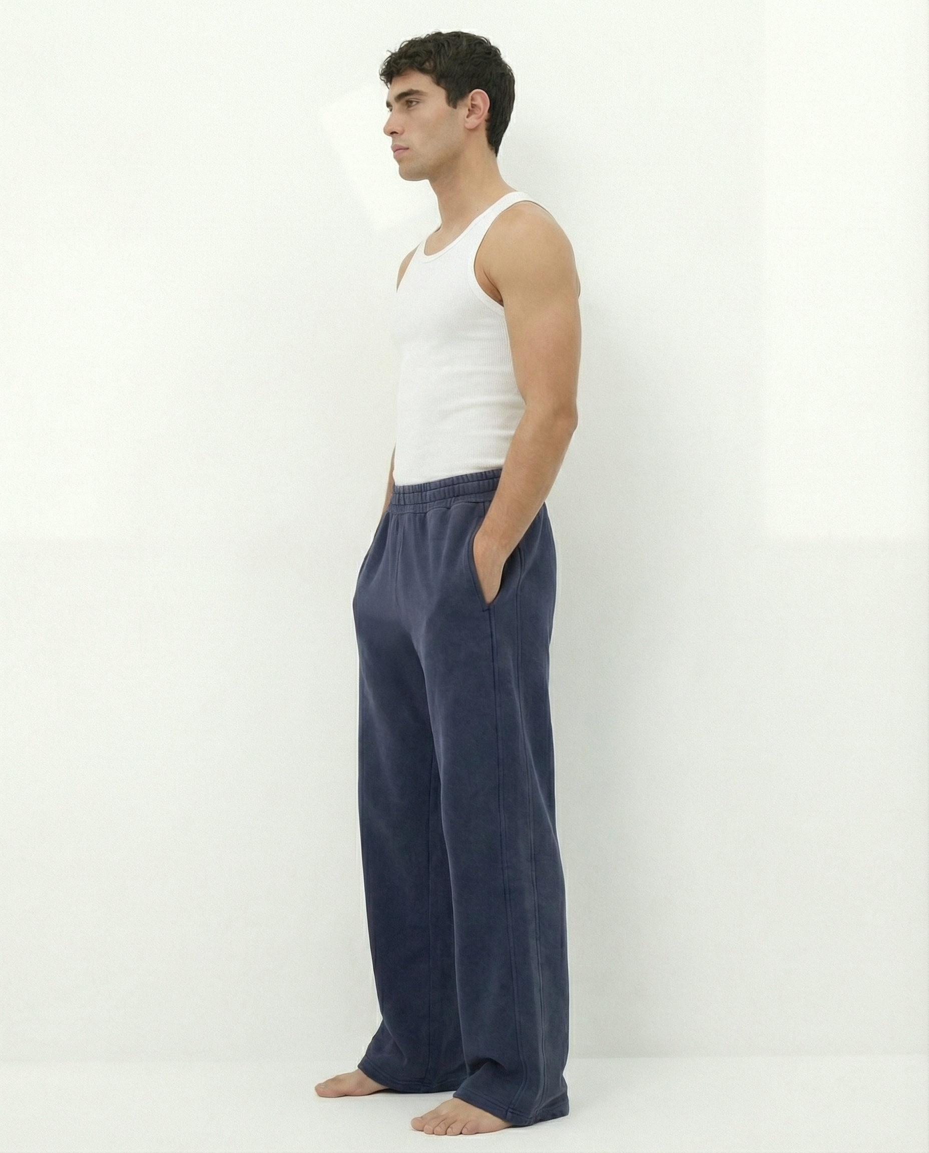 Man wearing a white tank top and blue acid wash pants against a white background