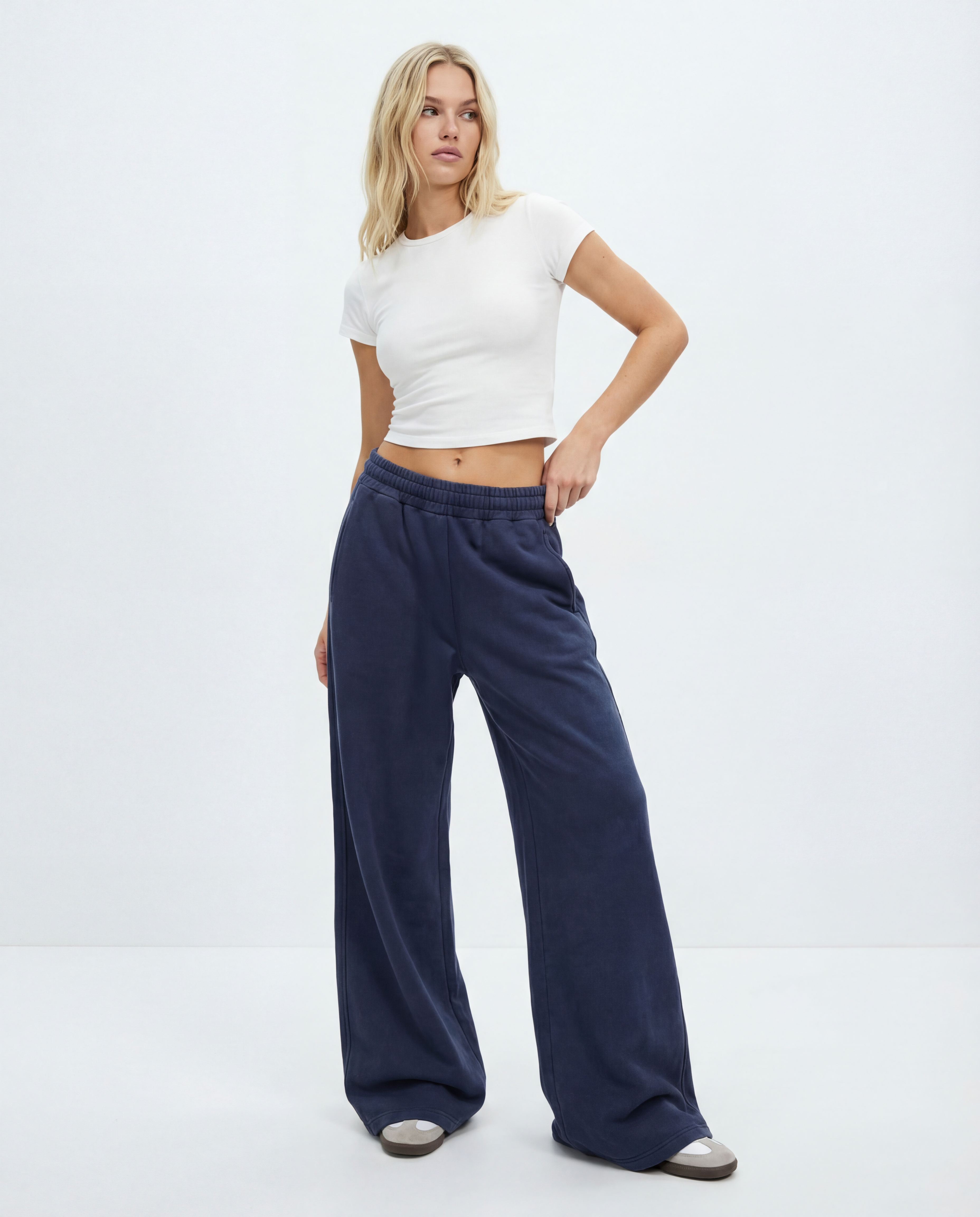 Woman wearing a white crop top and blue wide-leg acid wash pants on a white background