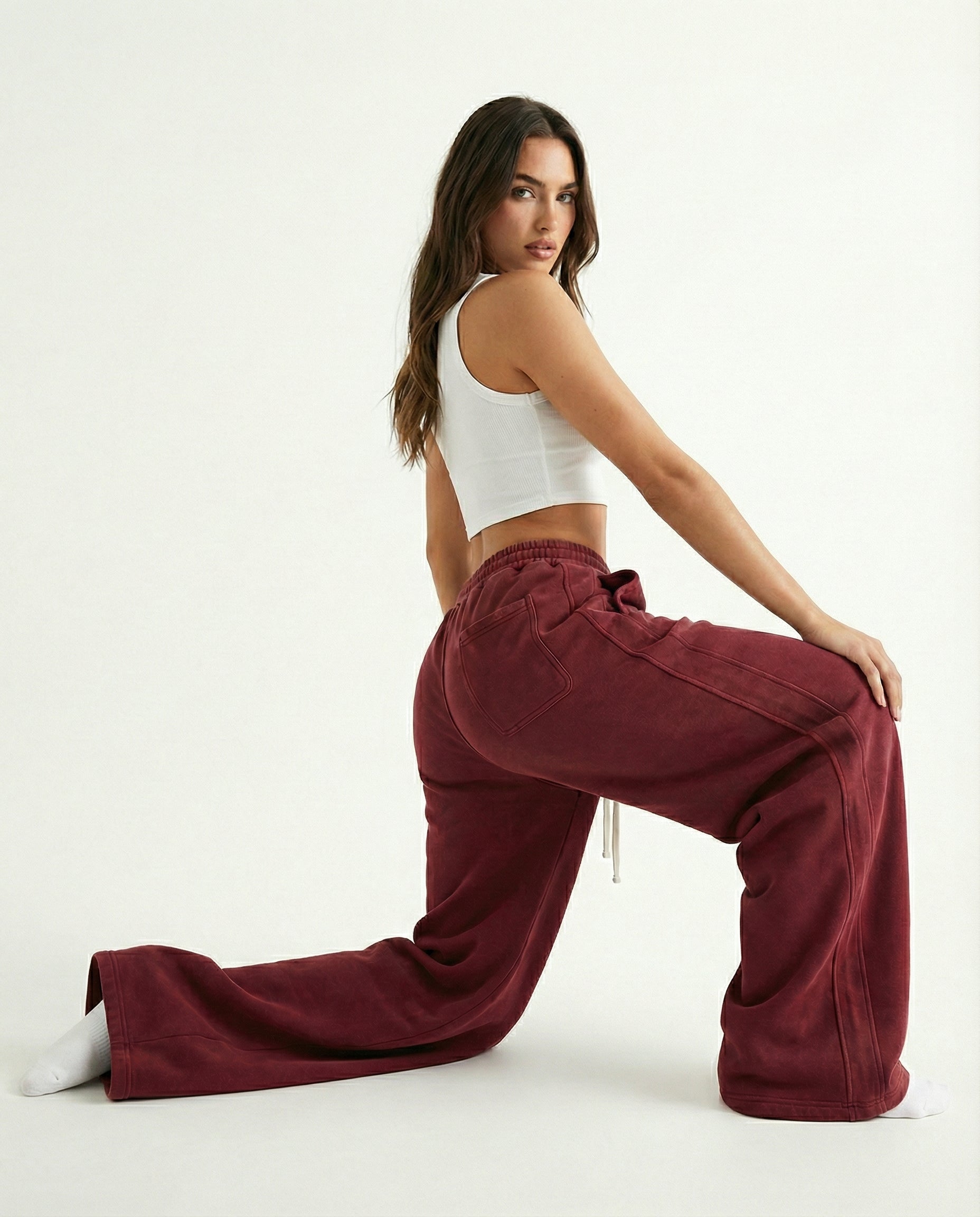 Woman wearing a white crop top and crimson red weatpants pants on a white background