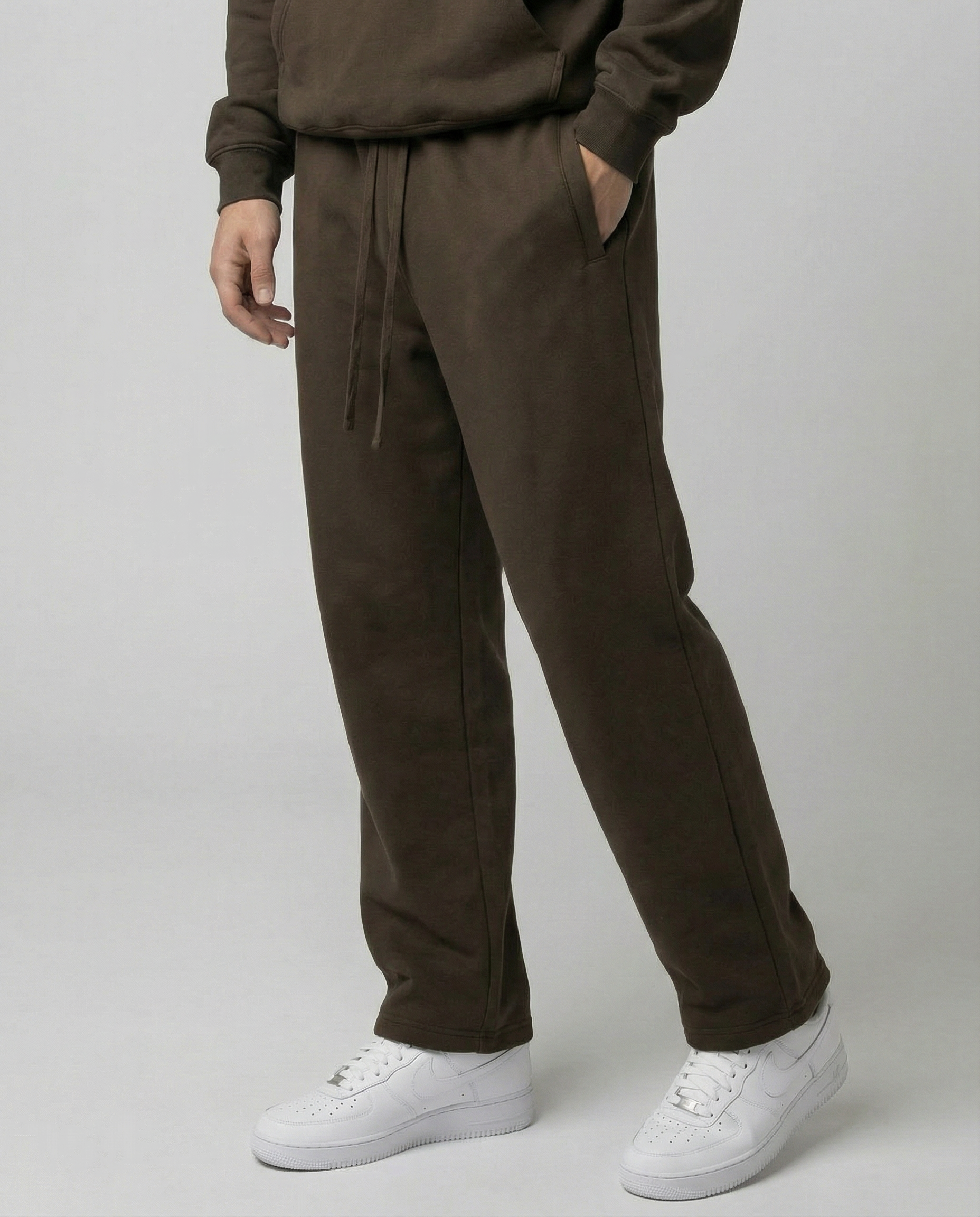 Person wearing brown tracksuit pants and white sneakers on a plain background