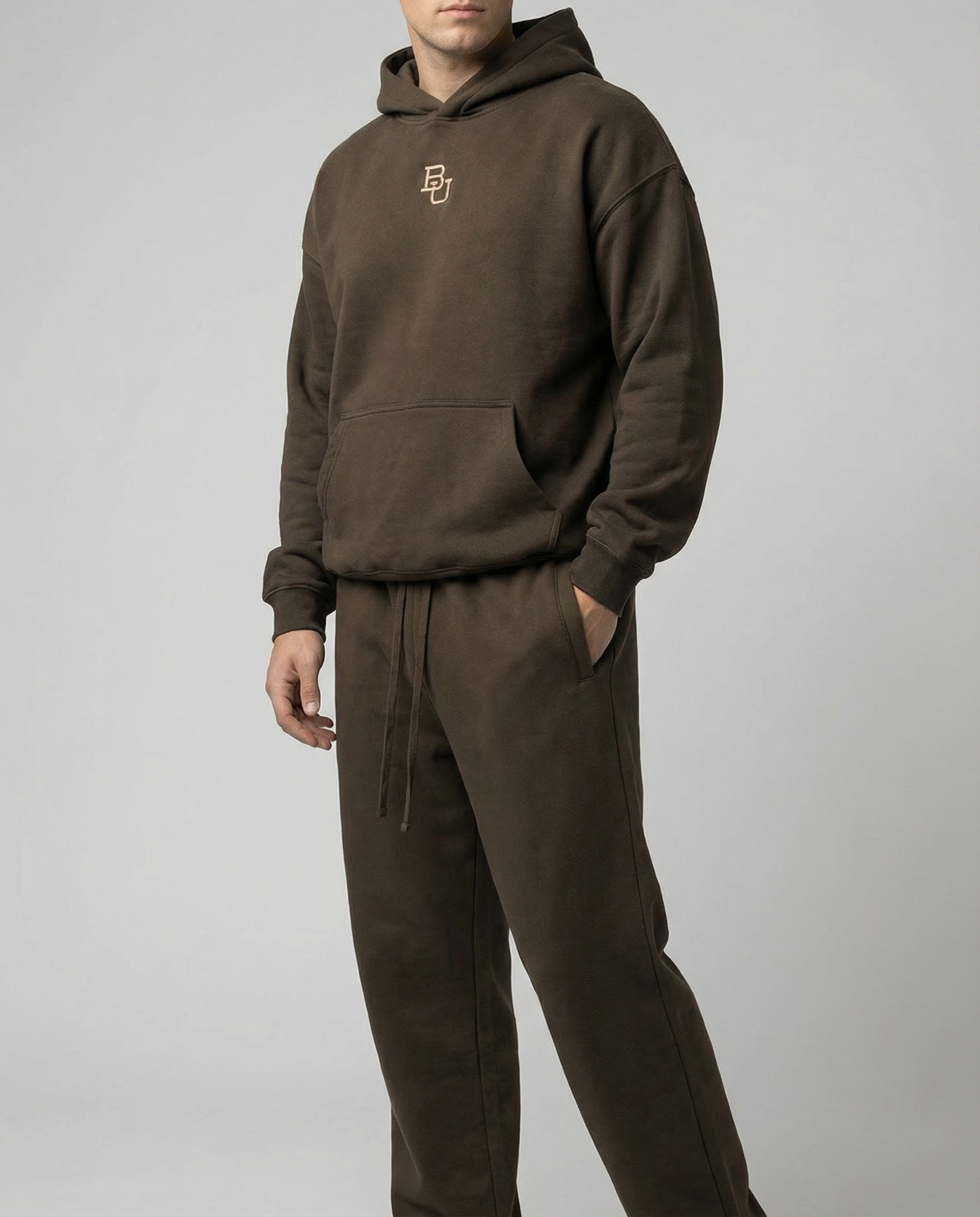 Person wearing a brown hoodie and pants with a logo on a gray background